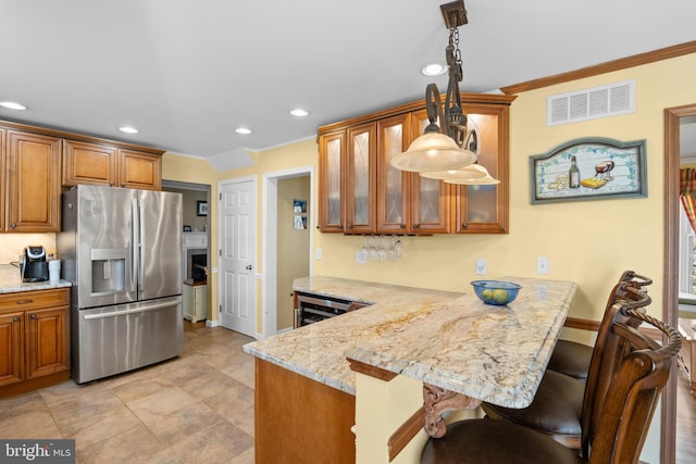 kitchen with a peninsula, brown cabinetry, stainless steel fridge with ice dispenser, and visible vents