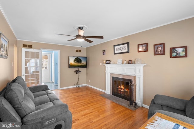 living area featuring visible vents, crown molding, baseboards, light wood-type flooring, and a tile fireplace