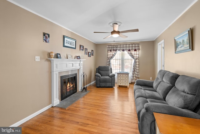 living area featuring light wood-type flooring, baseboards, a glass covered fireplace, and crown molding