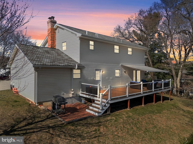 back of property at dusk with a lawn, a deck, and a chimney