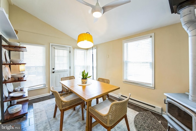 dining area featuring a ceiling fan, baseboards, a wood stove, vaulted ceiling, and baseboard heating