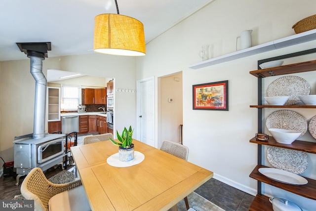 dining room featuring baseboards, lofted ceiling, and a wood stove