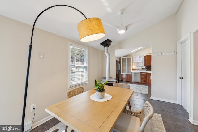 dining space featuring baseboards, lofted ceiling, a wood stove, and stone finish flooring