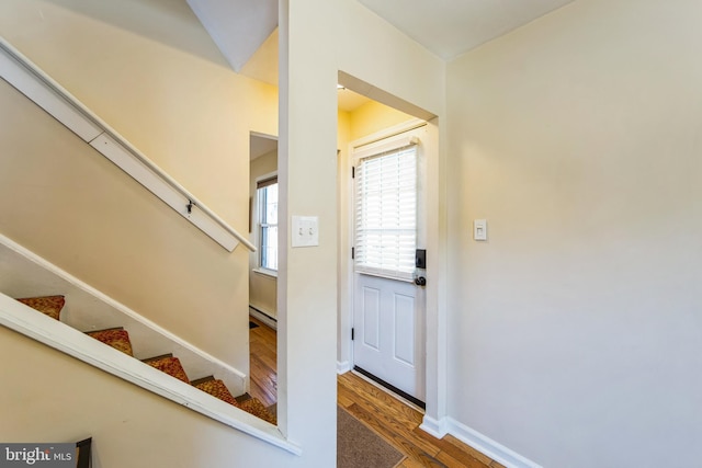 foyer entrance with stairs, a baseboard heating unit, baseboards, and wood finished floors