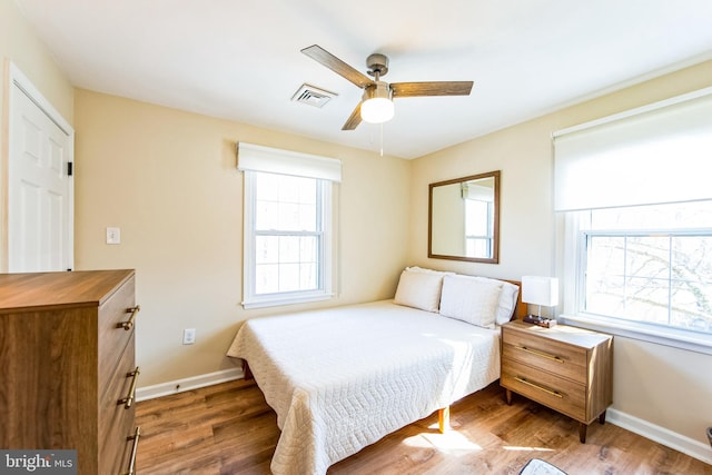 bedroom featuring ceiling fan, visible vents, baseboards, and wood finished floors