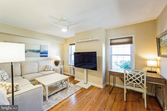 living area featuring baseboards, a healthy amount of sunlight, wood finished floors, and a ceiling fan