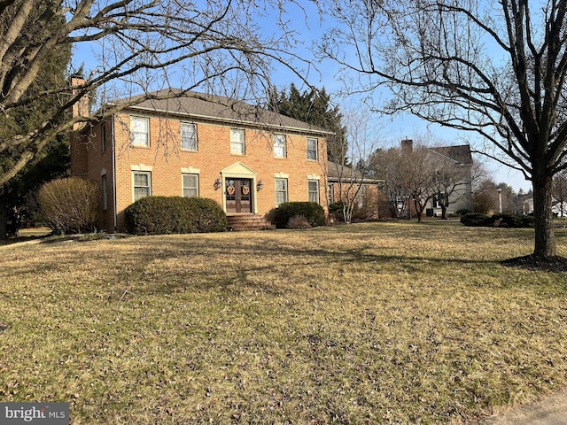 colonial-style house featuring brick siding, a chimney, and a front lawn