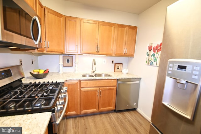 kitchen featuring light wood-style flooring, light stone countertops, stainless steel appliances, and a sink