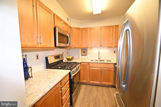 kitchen featuring light wood-type flooring, visible vents, a sink, stainless steel appliances, and light stone countertops