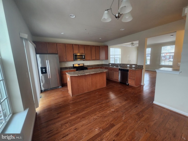 kitchen featuring a sink, dark wood-style floors, a center island, appliances with stainless steel finishes, and brown cabinetry