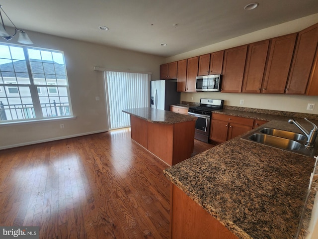 kitchen with brown cabinets, a sink, dark wood finished floors, a center island, and appliances with stainless steel finishes