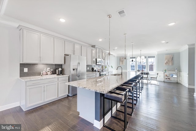 kitchen with ornamental molding, appliances with stainless steel finishes, a kitchen breakfast bar, dark wood-style floors, and a sink