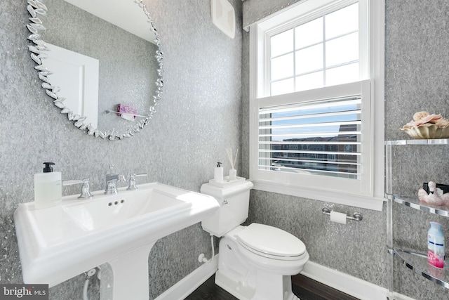 half bath with a sink, toilet, wood finished floors, and wallpapered walls