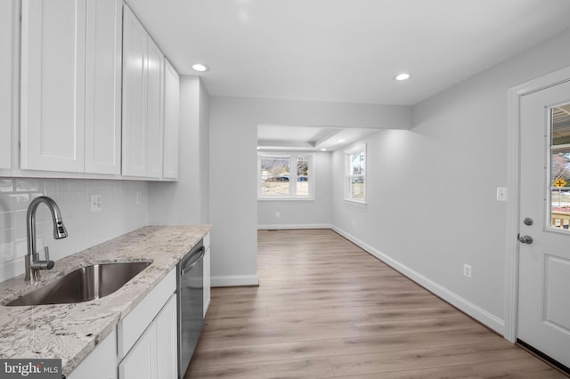 kitchen featuring light wood finished floors, a sink, decorative backsplash, white cabinets, and dishwasher