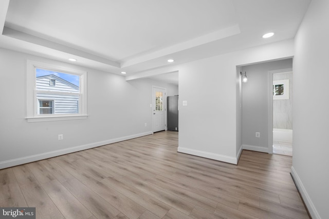 spare room featuring recessed lighting, baseboards, a raised ceiling, and light wood-style floors