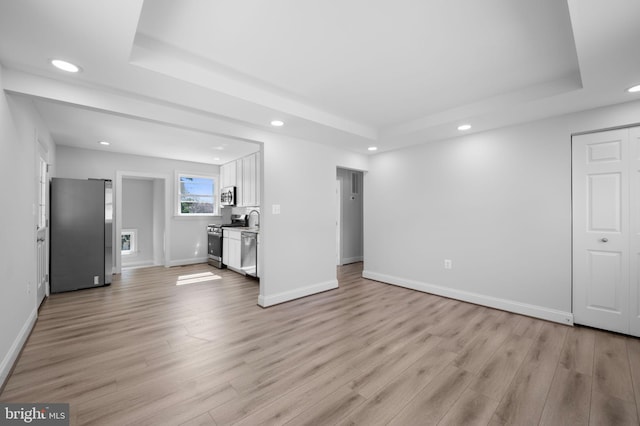 unfurnished living room featuring a tray ceiling, recessed lighting, and light wood-type flooring