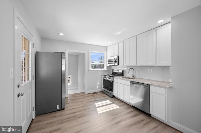 kitchen with white cabinets, tasteful backsplash, light wood-type flooring, and appliances with stainless steel finishes