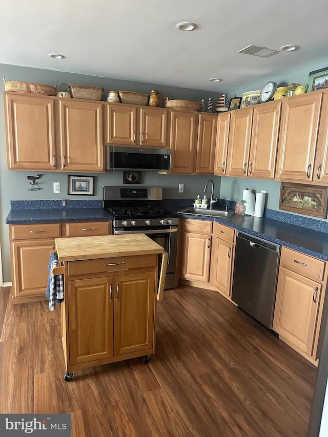 kitchen with a sink, dark wood-style flooring, appliances with stainless steel finishes, and light brown cabinetry