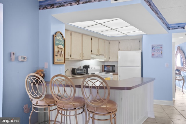 kitchen featuring under cabinet range hood, decorative backsplash, a peninsula, cream cabinetry, and white appliances