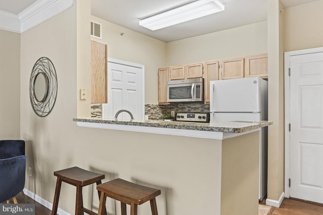 kitchen with light brown cabinets, visible vents, a breakfast bar, stainless steel microwave, and backsplash