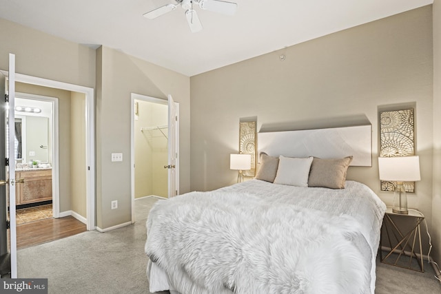 carpeted bedroom with ensuite bath, a spacious closet, a ceiling fan, and baseboards