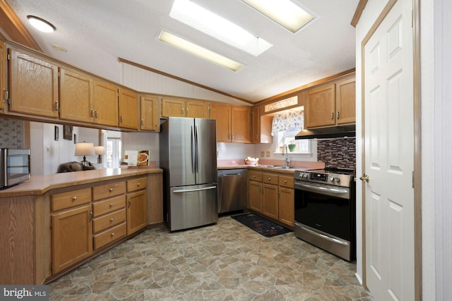 kitchen featuring brown cabinetry, a sink, stainless steel appliances, vaulted ceiling, and under cabinet range hood