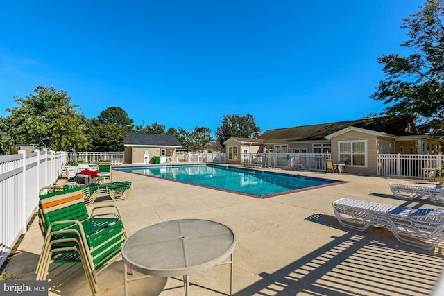 pool with an outbuilding, a patio area, and fence