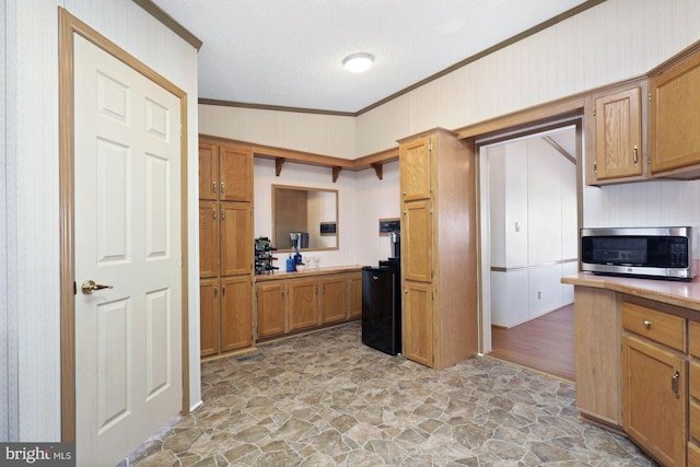 kitchen with stainless steel microwave, stone finish flooring, crown molding, light countertops, and brown cabinets