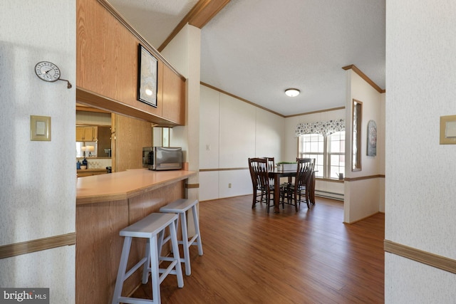 kitchen with a breakfast bar area, wood finished floors, a baseboard radiator, ornamental molding, and stainless steel microwave