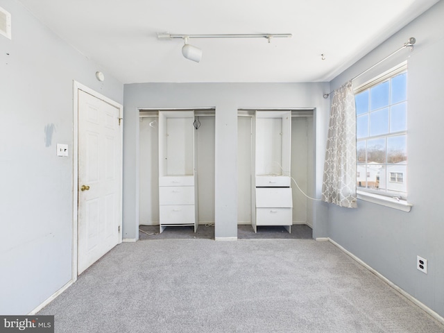 unfurnished bedroom with carpet, visible vents, baseboards, track lighting, and multiple closets