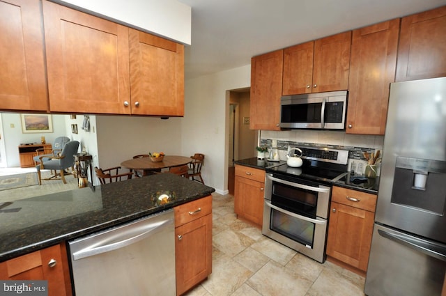 kitchen with decorative backsplash, appliances with stainless steel finishes, brown cabinetry, and dark stone counters