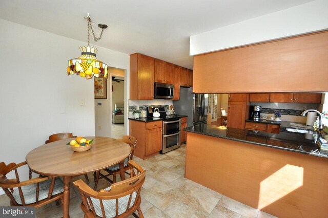 kitchen featuring brown cabinetry, stainless steel appliances, dark countertops, and a sink