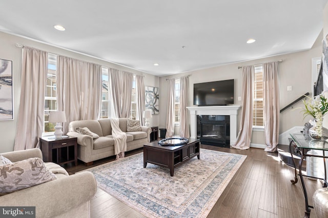 living room featuring plenty of natural light, dark wood-type flooring, and a glass covered fireplace