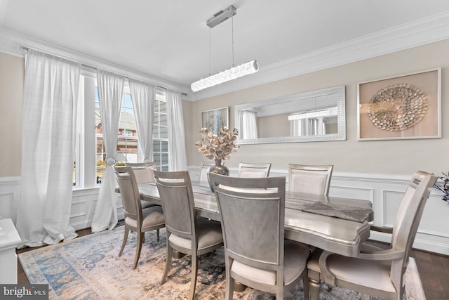 dining room with a wainscoted wall, ornamental molding, a decorative wall, and wood finished floors