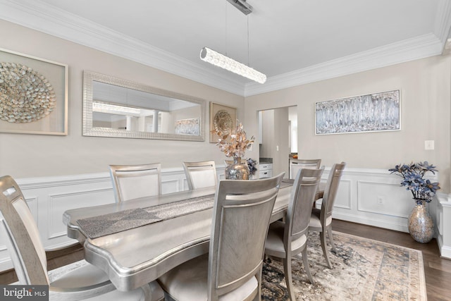 dining area with a decorative wall, a wainscoted wall, crown molding, and dark wood-type flooring