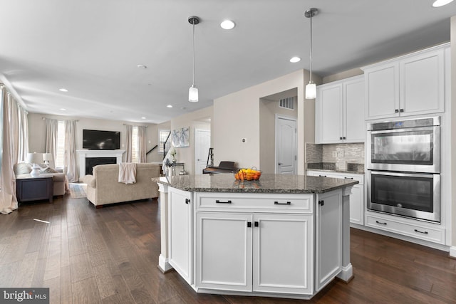 kitchen with dark wood finished floors, double oven, a fireplace, and white cabinetry