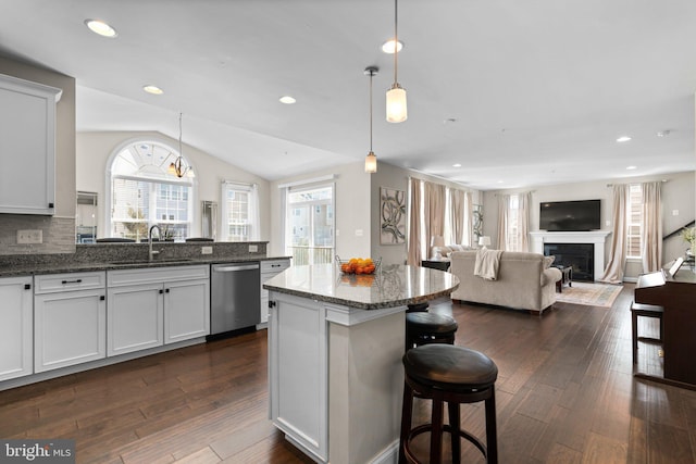 kitchen with stainless steel dishwasher, dark stone counters, a fireplace, dark wood-style flooring, and vaulted ceiling