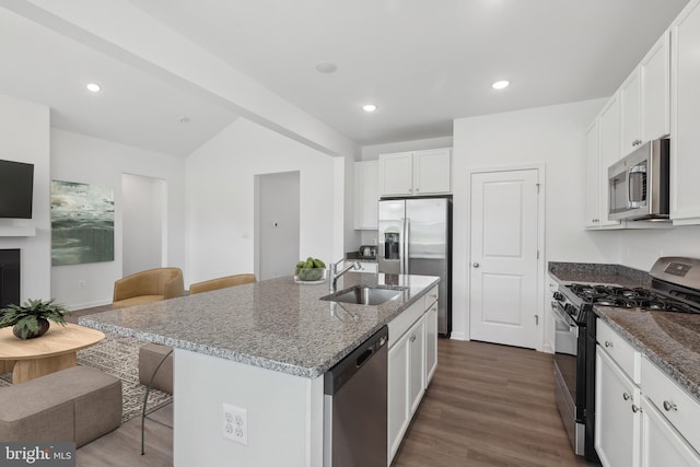 kitchen featuring a breakfast bar, a sink, dark stone countertops, appliances with stainless steel finishes, and dark wood-style flooring