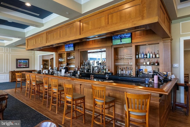 bar featuring a bar, beam ceiling, wood finished floors, and ornamental molding