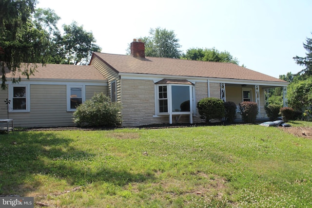 view of front of property with a front lawn, stone siding, roof with shingles, and a chimney