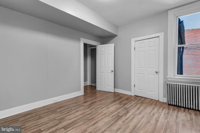 unfurnished bedroom featuring baseboards, wood finished floors, and radiator heating unit