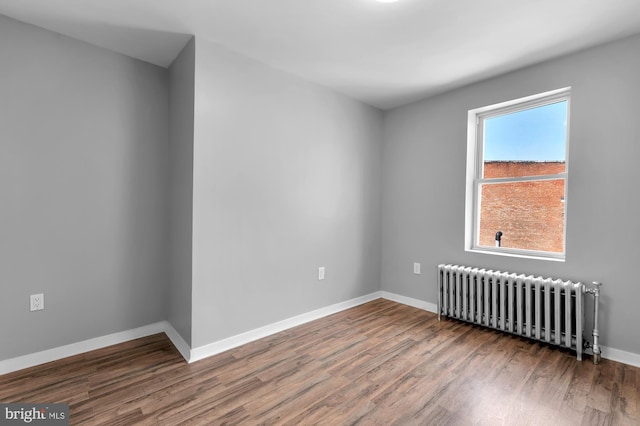 empty room with baseboards, radiator, and wood finished floors