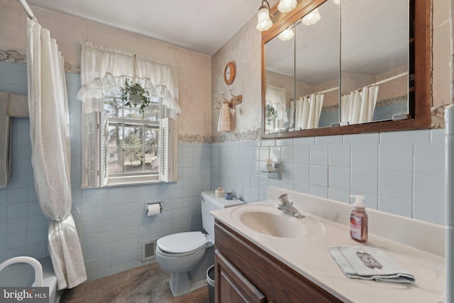 bathroom featuring visible vents, toilet, tile walls, wainscoting, and vanity