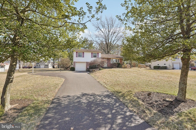 tri-level home with a front lawn, brick siding, a garage, and driveway