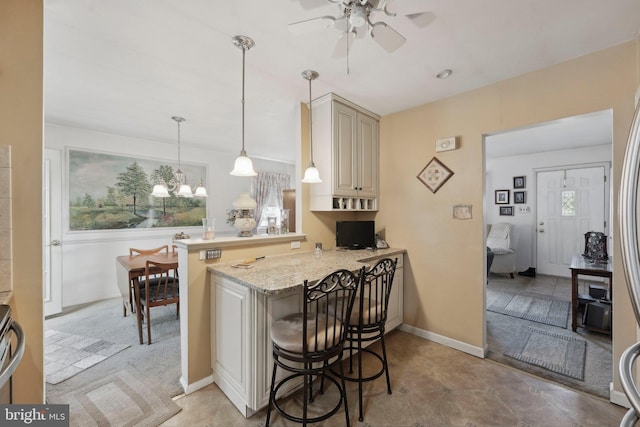 kitchen with light stone countertops, pendant lighting, a breakfast bar, a peninsula, and a ceiling fan