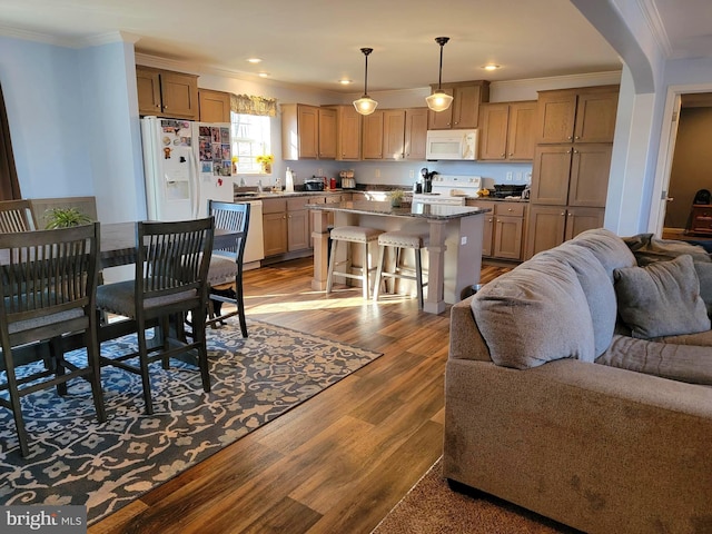 kitchen with white appliances, a breakfast bar area, dark wood-style flooring, crown molding, and open floor plan