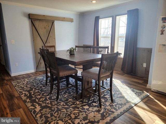 dining area featuring baseboards, a barn door, ornamental molding, wainscoting, and wood finished floors