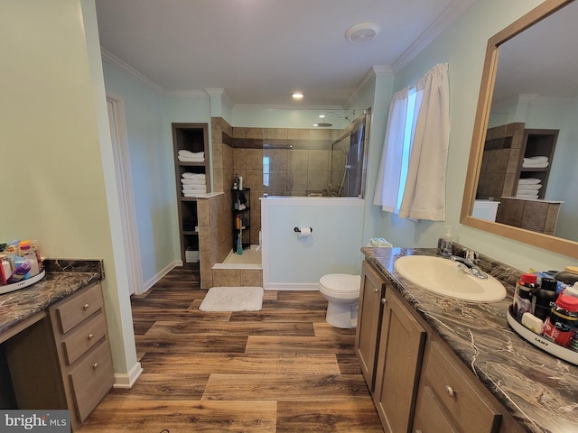 bathroom featuring vanity, wood finished floors, a walk in shower, crown molding, and toilet