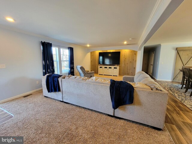 living area with visible vents, wood finished floors, baseboards, and ornamental molding