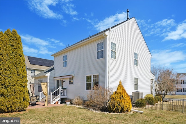 rear view of house featuring central air condition unit, a lawn, and fence